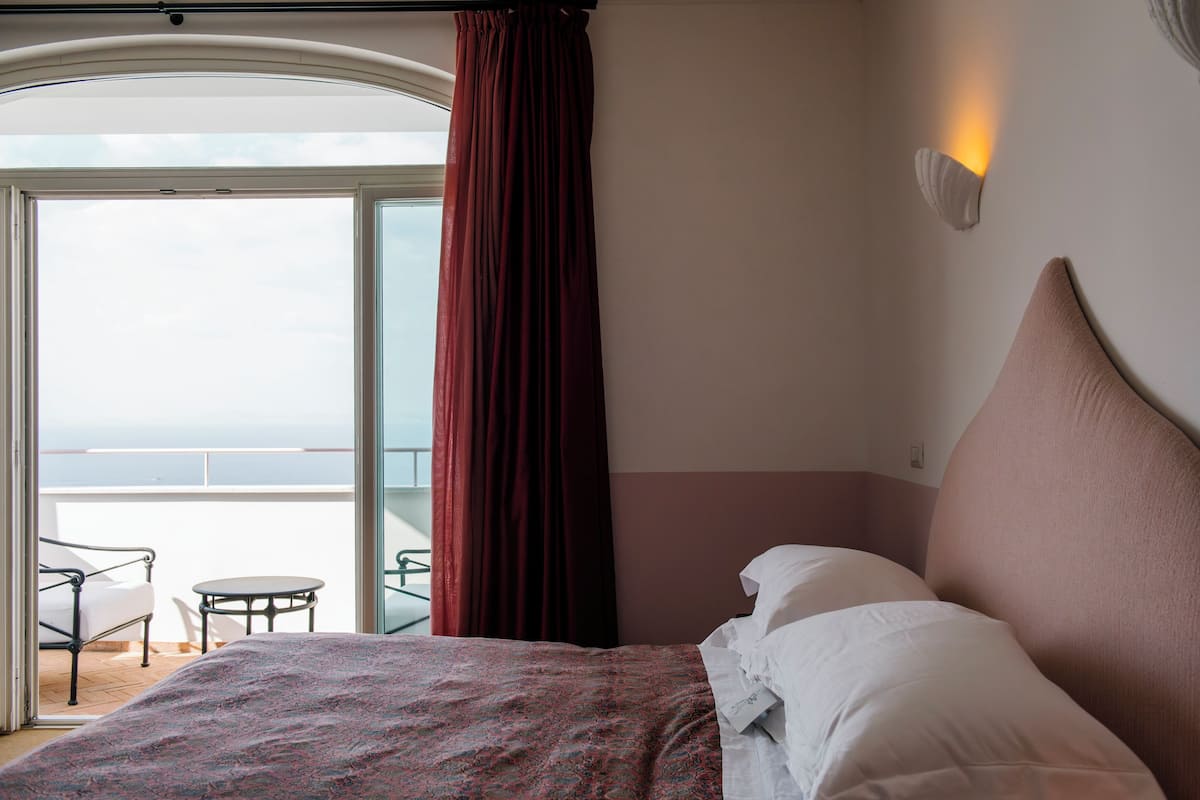 A hotel room with a bed, a view of the balcony, and a table with chairs.
