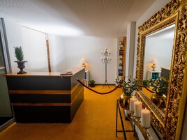 Un mostrador de recepción con una planta en maceta, una lámpara de pie y un espejo con un marco ornamentado.