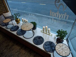 Una mesa con objetos decorativos y velas, una planta pequeña y una ventana con vista a la calle.