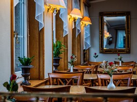 Un interior de restaurante con mesas y sillas de madera, plantas en macetas y lámparas de pared.