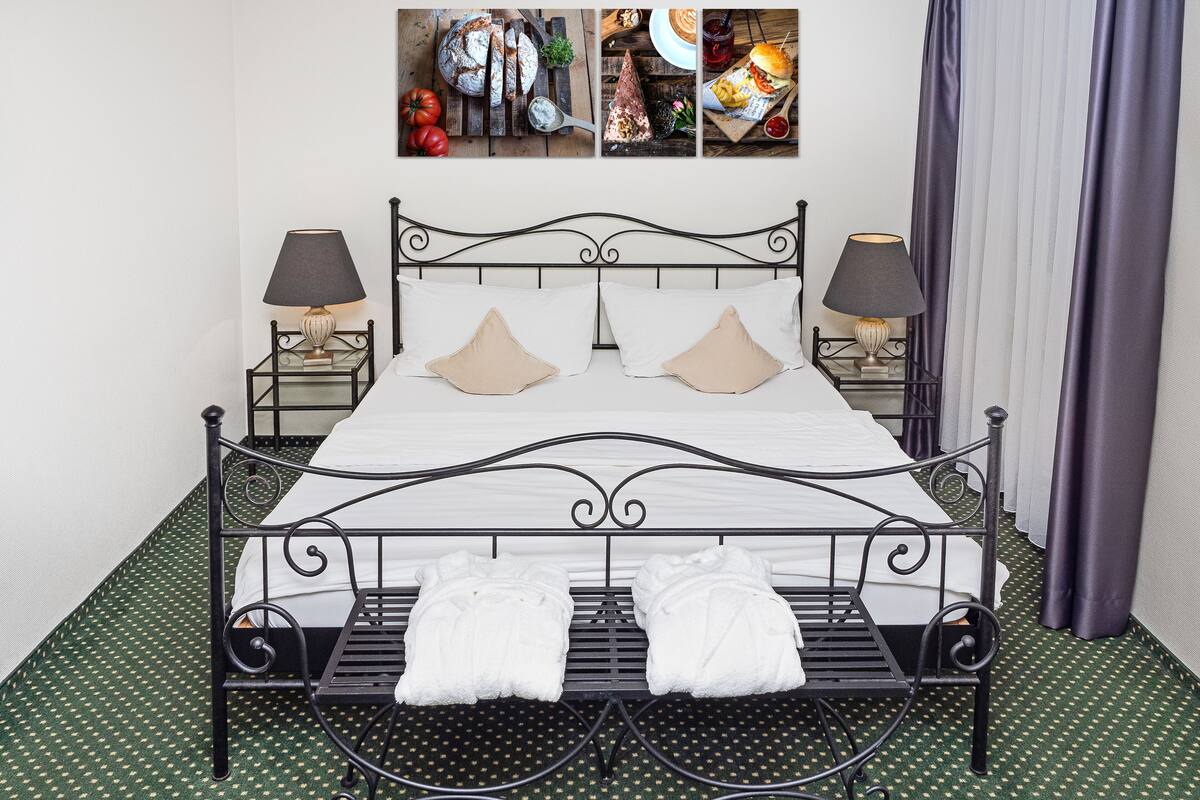 A neatly made bed with white linens and two pillows, flanked by two bedside tables with lamps, in a room with a green patterned carpet.