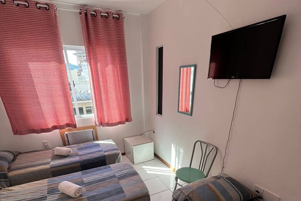 Habitación de hotel con tres camas, una televisión de pantalla plana y una ventana con cortinas rojas.