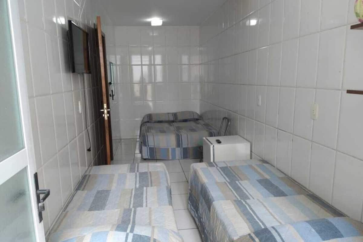 Una habitación pequeña y funcional con dos camas, un televisor en la pared y una mesita.