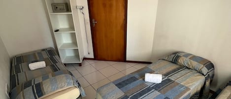 A small, tidy room with two beds, a chair, and a wooden door.