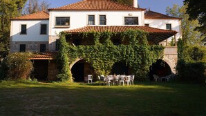 A two-story house with a tiled roof, stone arches, and a covered outdoor seating area with chairs and tables. - Lugar da Pedra Alta (Gouveia)