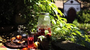 A picnic setup with a glass jar, a plate with food, and a glass of drink, surrounded by greenery and a small building in the background. - Lugar da Pedra Alta (Gouveia)