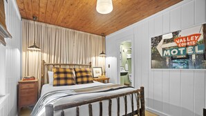 Ein Schlafzimmer mit einem hölzernen Bett, einem Nachttisch, einer Lampe und einem an der Wand befestigten Schild für das Valley Courts Motel.