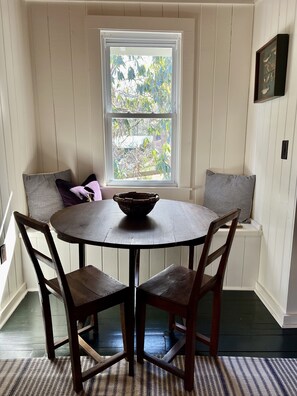 A dining area with a round table, four wooden chairs, and a window with a view of trees.