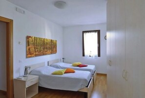 Two single beds with colorful pillows, a large abstract painting, and a functional workspace.