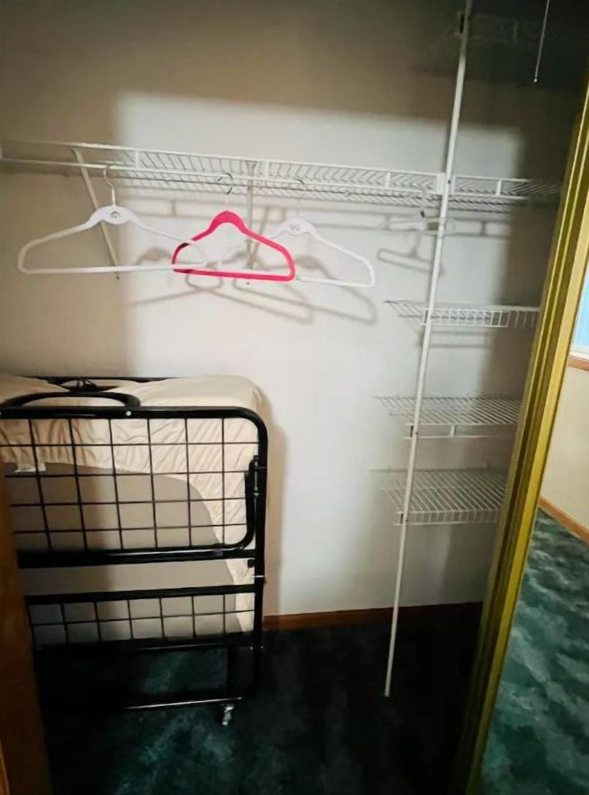 A closet with a metal rack holding white and pink hangers, a black metal storage unit, and a white shelving unit.