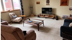 Ein Wohnzimmer mit Sofa, Sessel, Couchtisch, Fernsehtisch und Dekorationselementen.