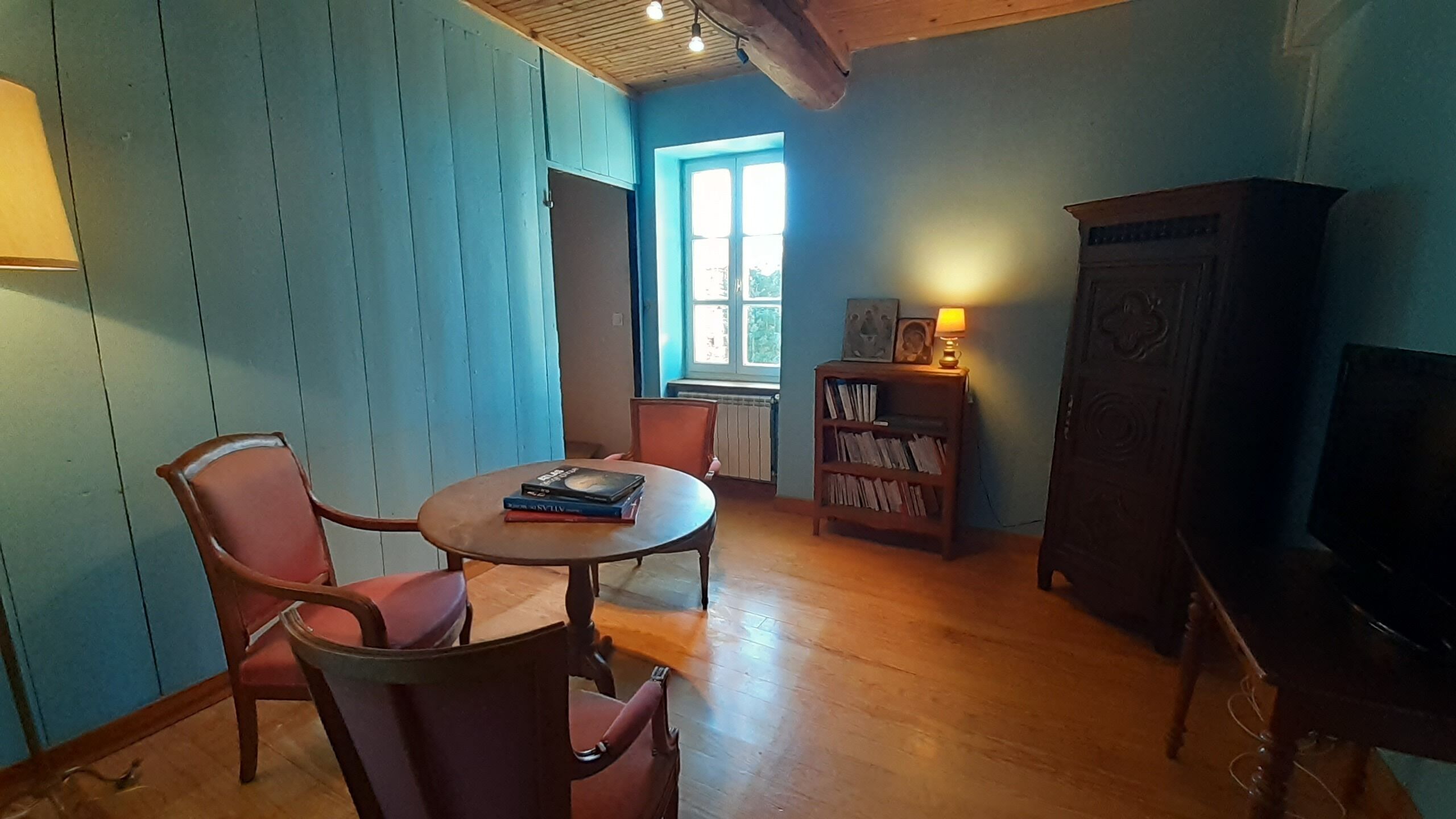 A cozy room with a round table, two chairs, a bookshelf, a lamp, and a television.