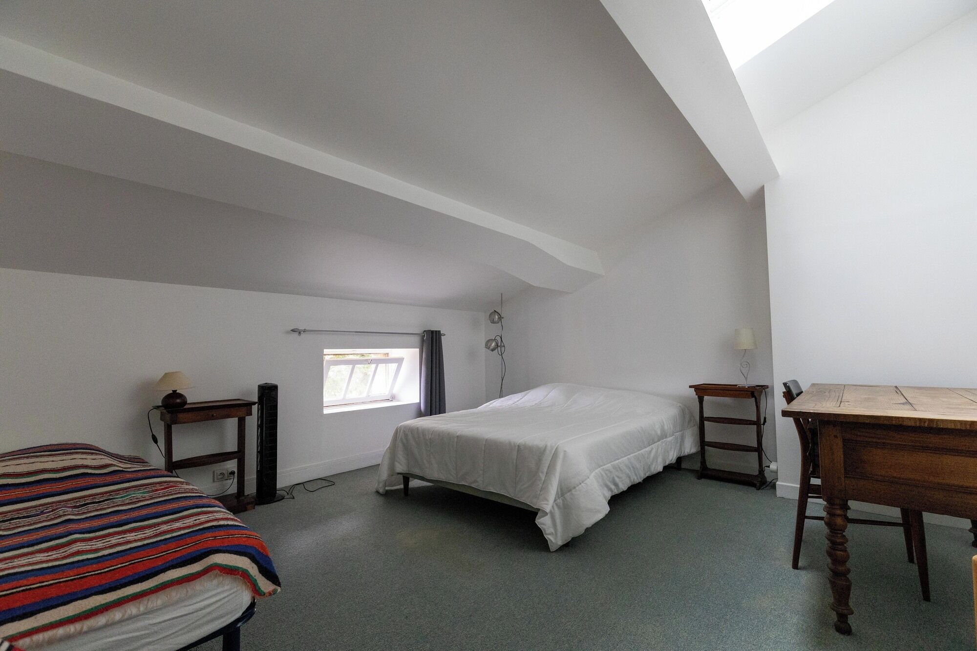 A bedroom with a bed, a desk, and a window.
