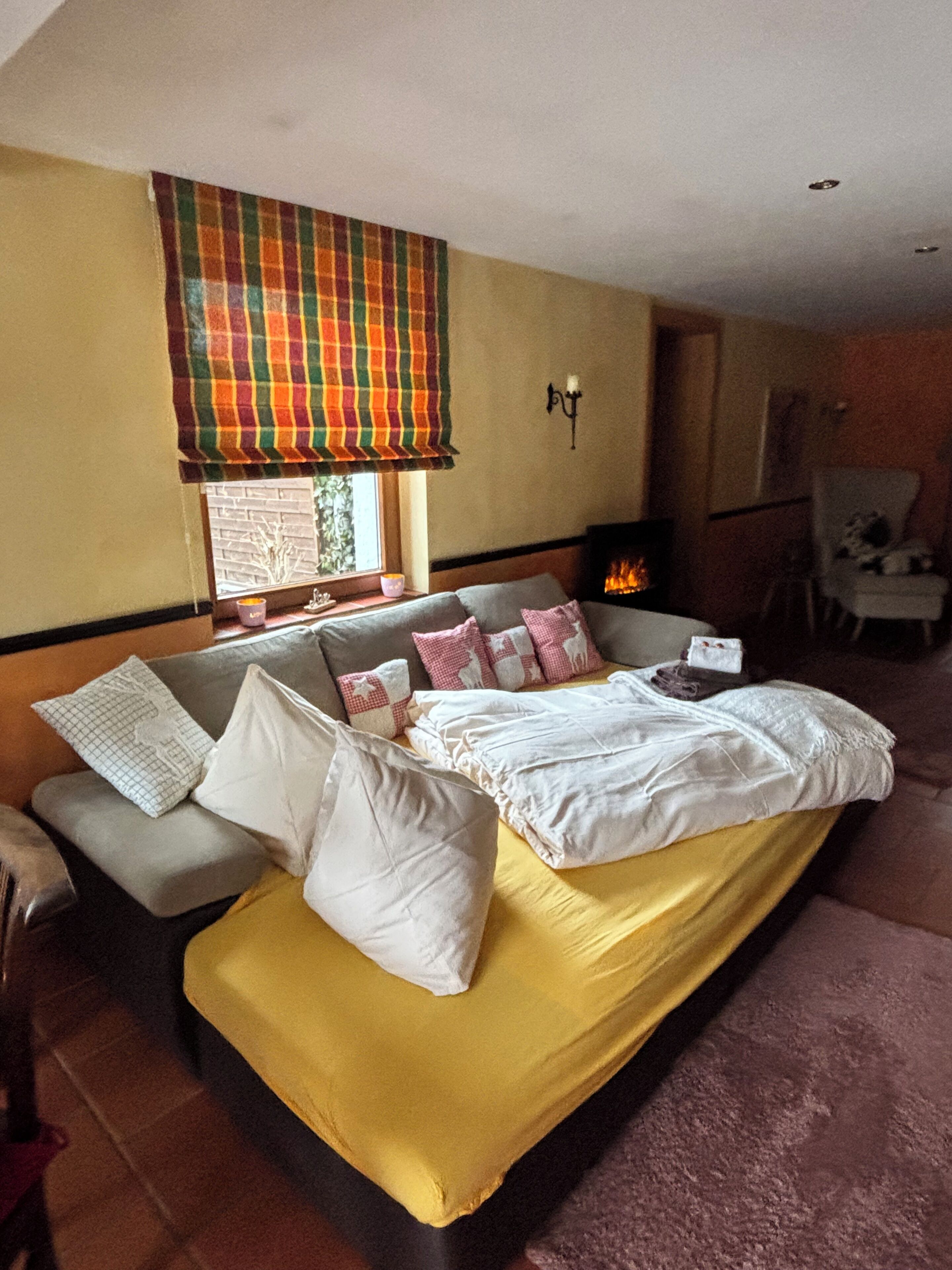 A modern bedroom with a sofa bed, a fireplace, and a window with a colorful curtain.