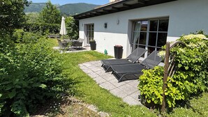 A house with a patio, a table, chairs, and a sun lounger.