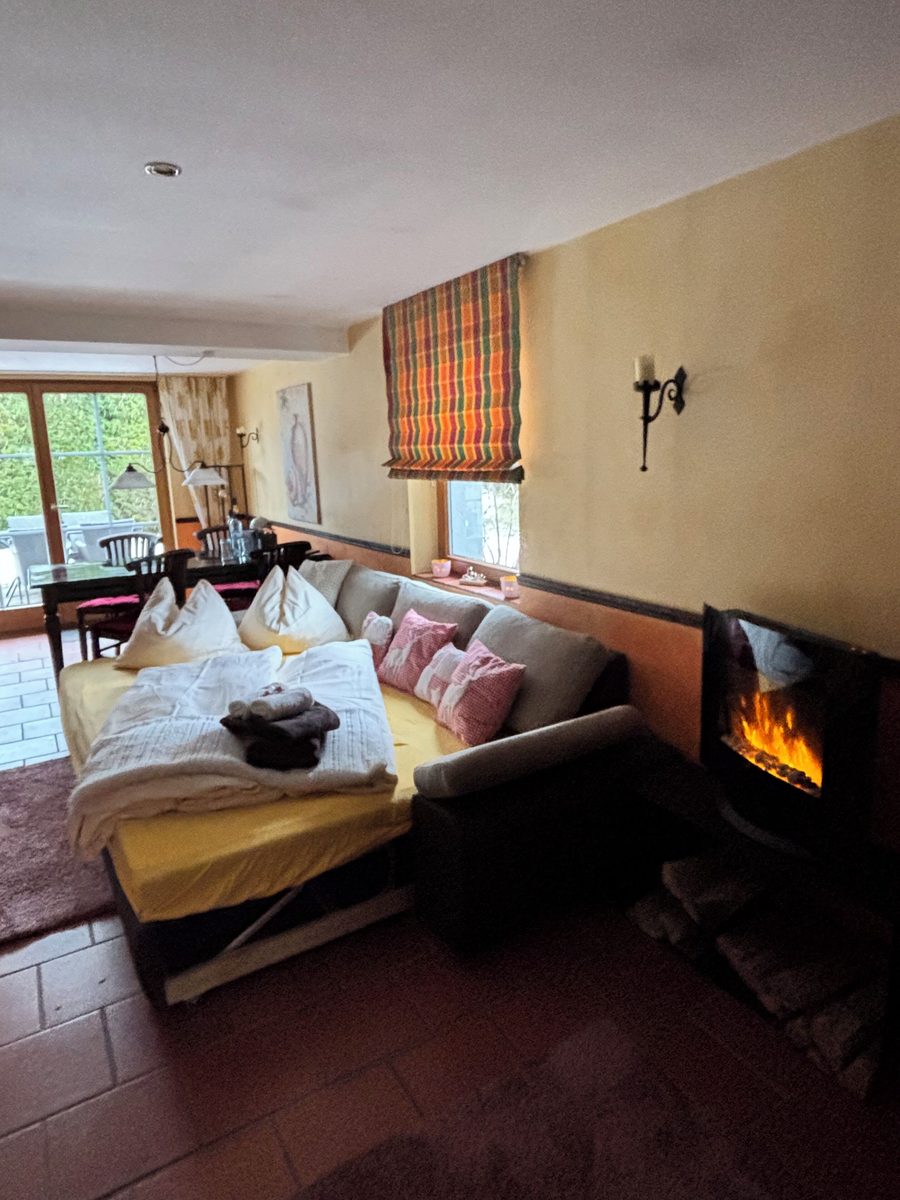A cozy room with a bed, a sofa, a fireplace, and a dining area with a table and chairs.