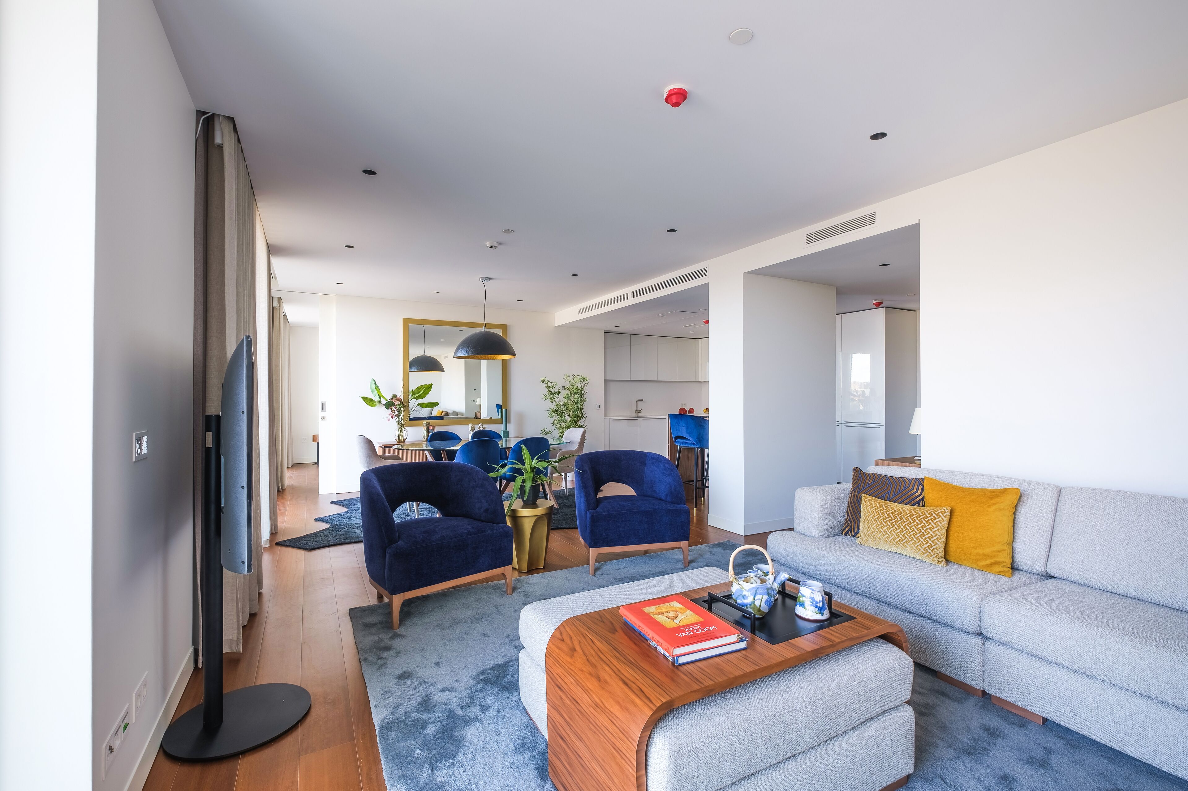 Una sala de estar moderna con un sofá gris, sillones azules, una mesa de centro de madera y un televisor de pantalla plana.