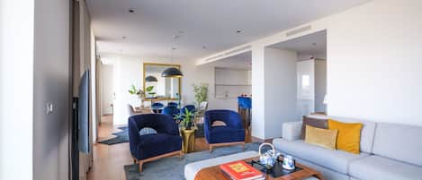 A modern living room with a grey sofa, blue armchairs, a wooden coffee table, and a flat-screen TV.