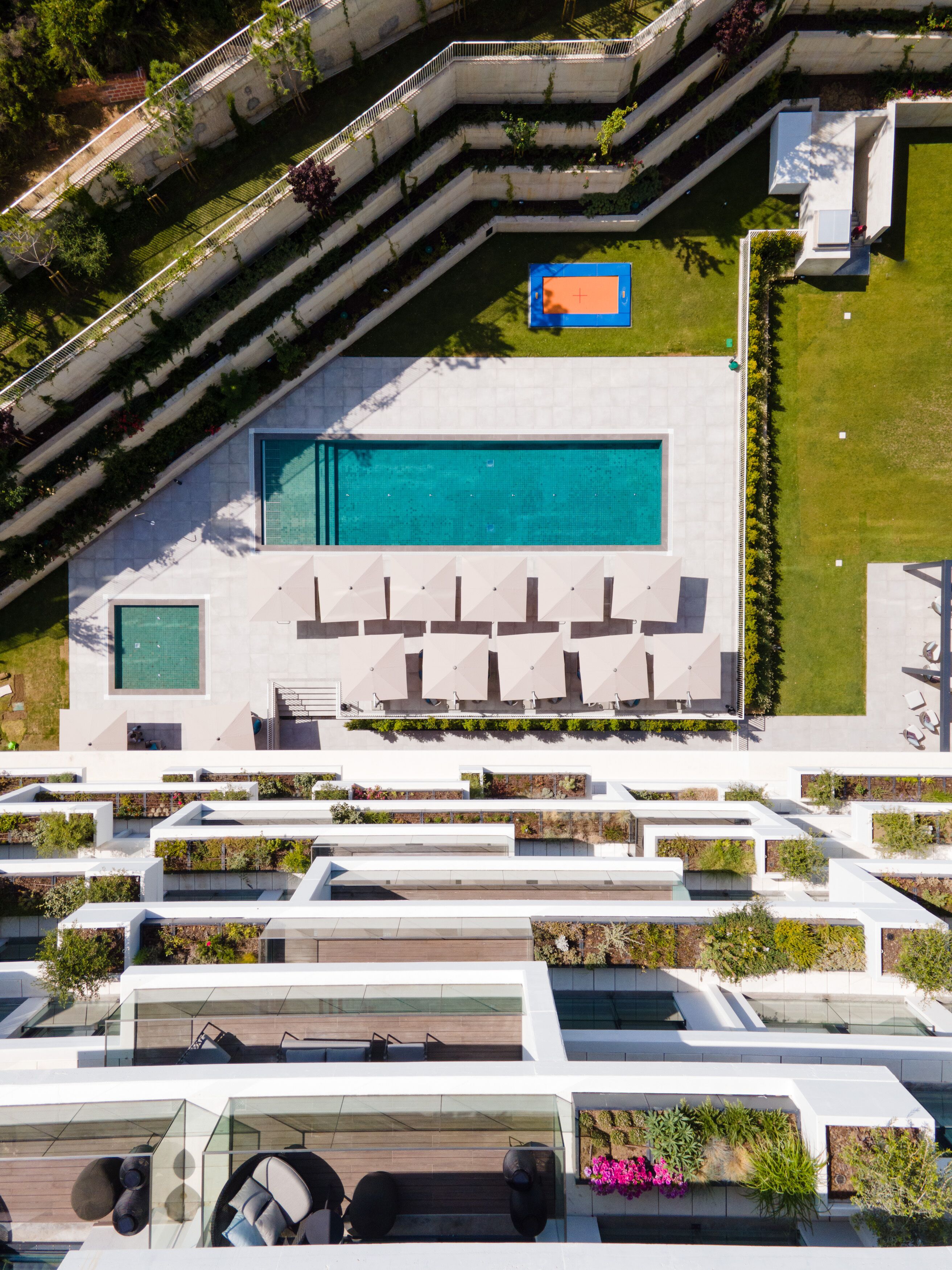 Luchtbeeld van een modern gebouw met een zwembad, terrasmeubilair en aangelegde terrassen.