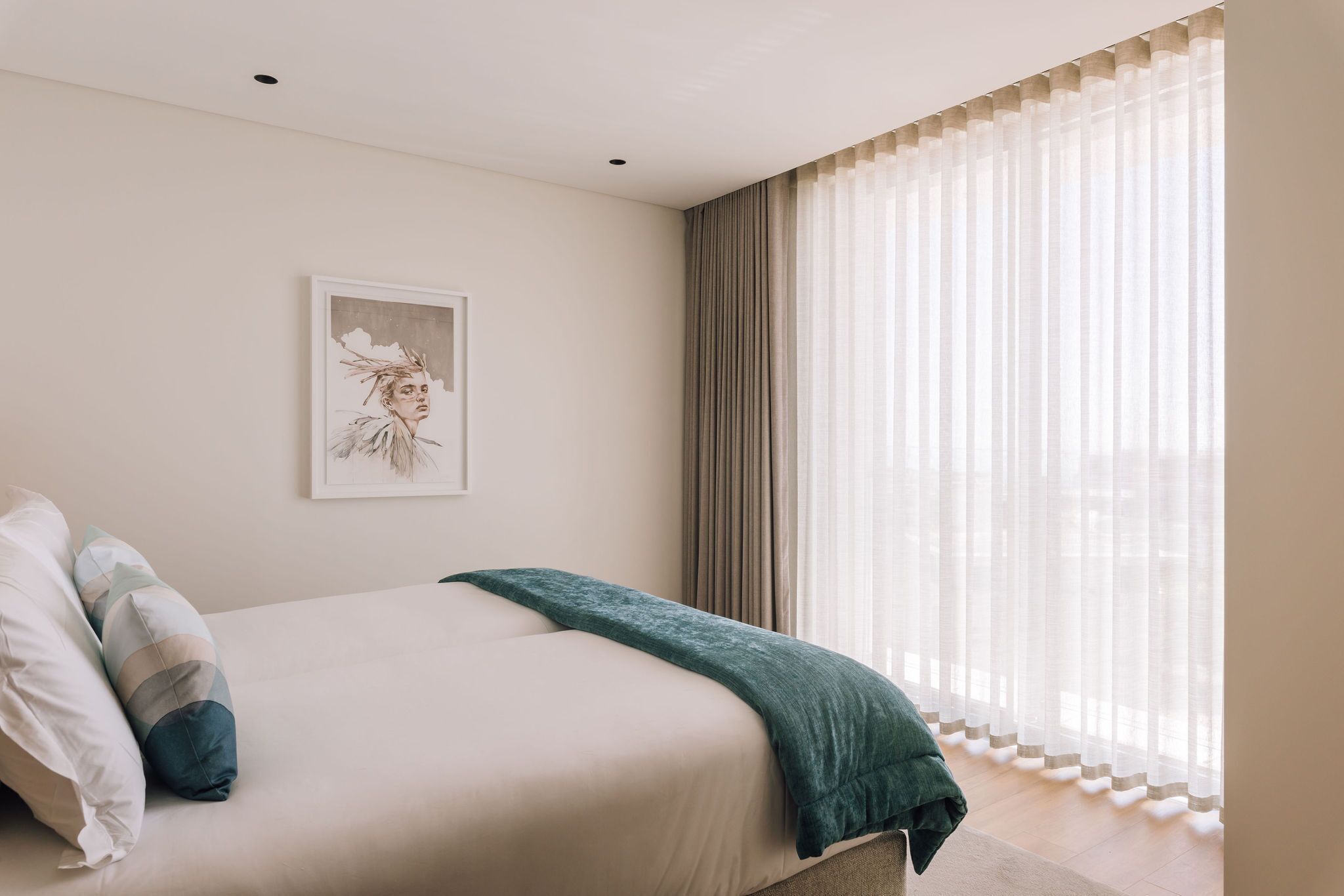 Une chambre à coucher avec un lit, une œuvre d’art encadrée au mur et des rideaux légers à la fenêtre.