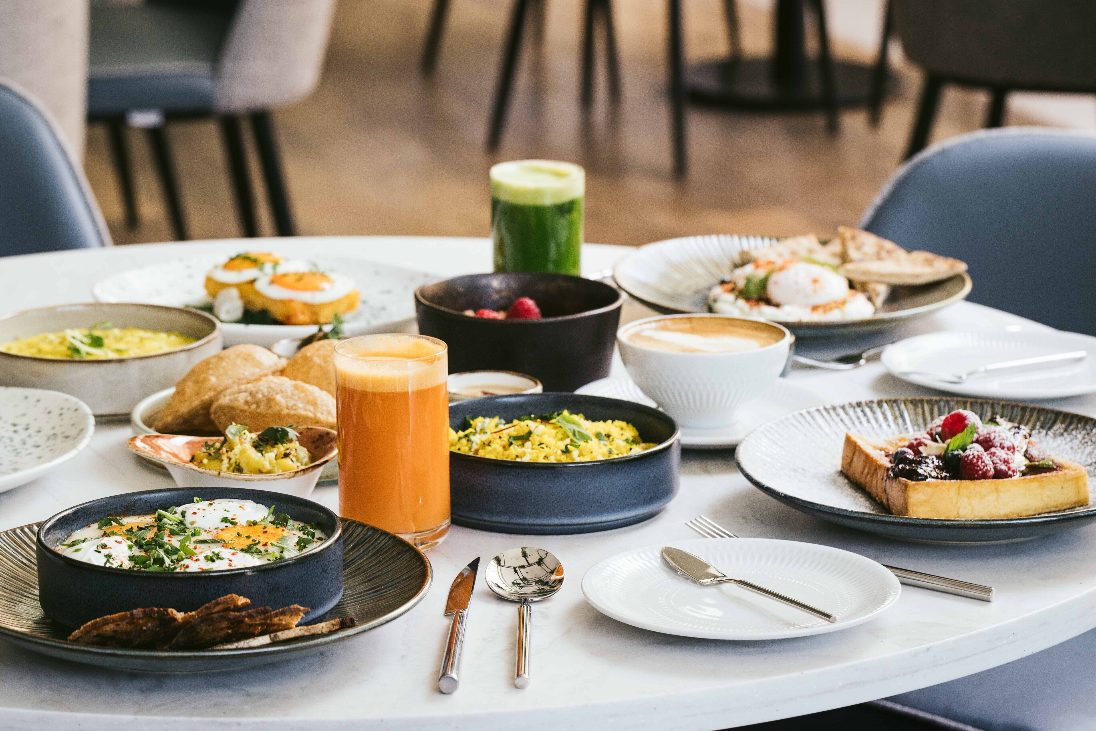 Una mesa servida con diversos platos, incluyendo un tazón de sopa, un plato de huevos y un vaso de jugo.