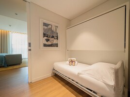Quarto moderno com uma cama de solteiro, piso de madeira, janela grande com cortinas e um quadro na parede.