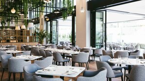 A spacious restaurant with high ceilings, hanging plants, and large windows offering a view of the city. - Martinhal Lisbon Oriente (Lisbon)