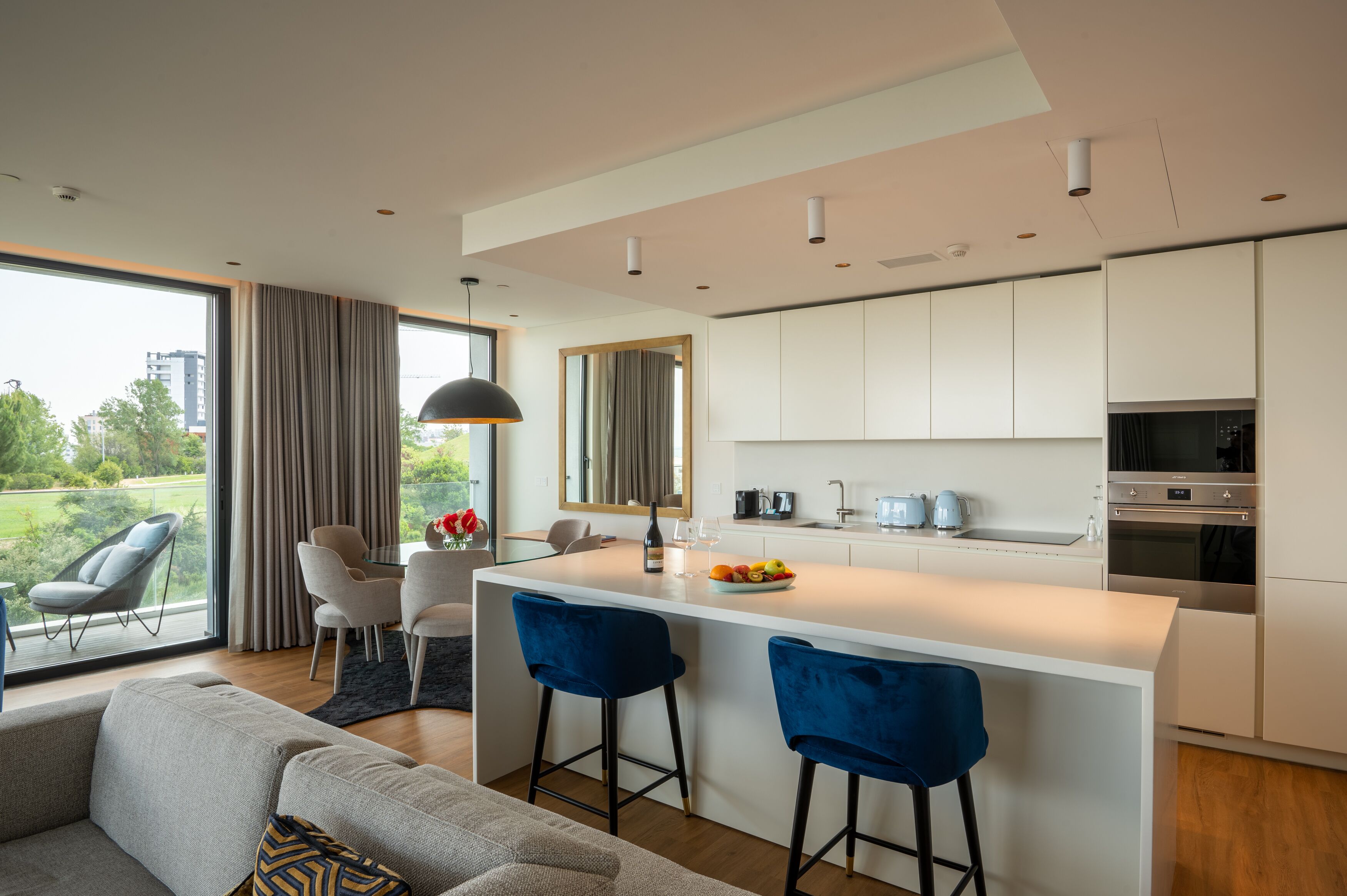 Una cocina moderna con una isla central, armarios blancos y una zona de comedor con dos taburetes azules.