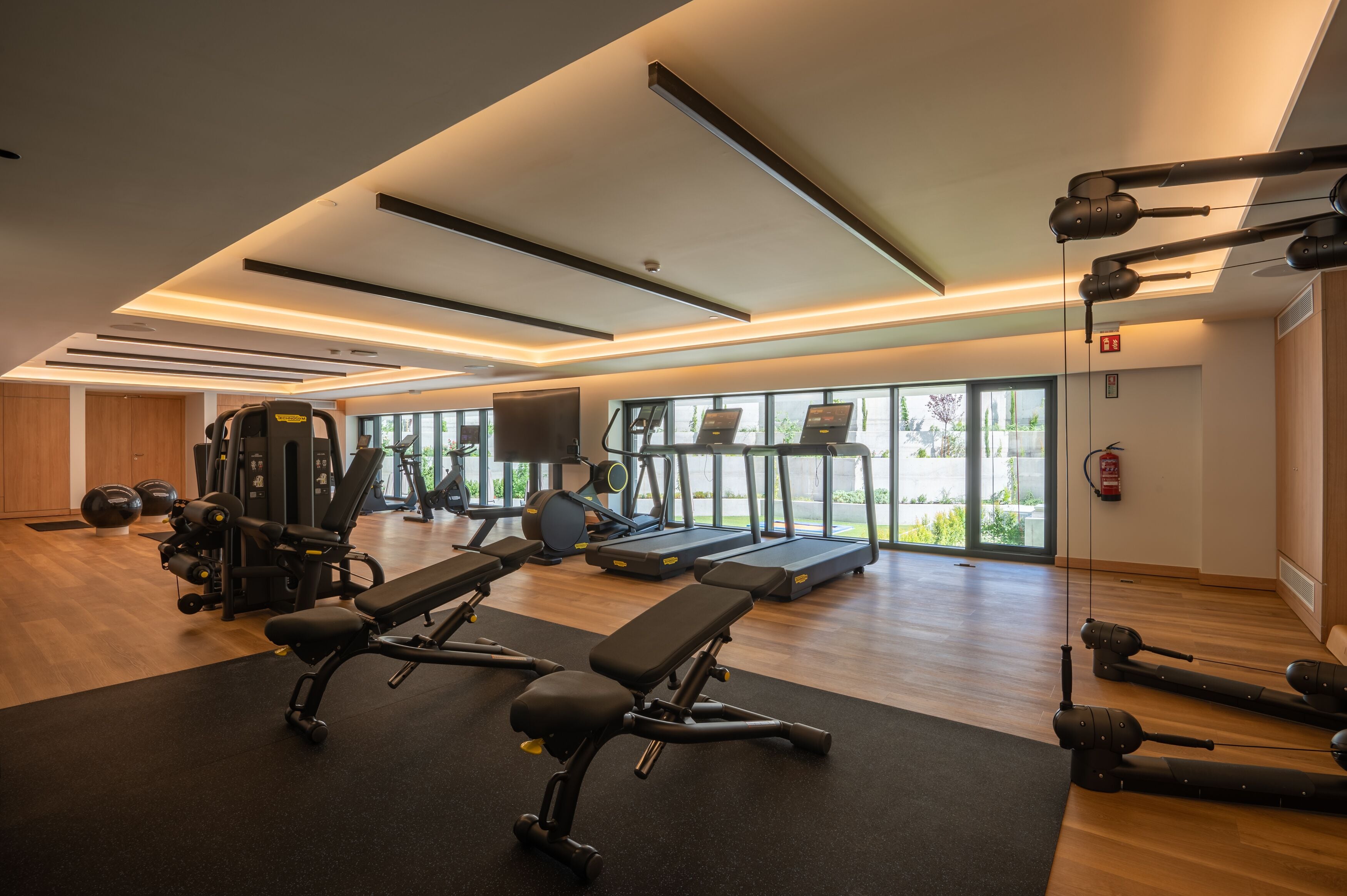 A modern gym with exercise equipment, treadmills, and a large window providing natural light.