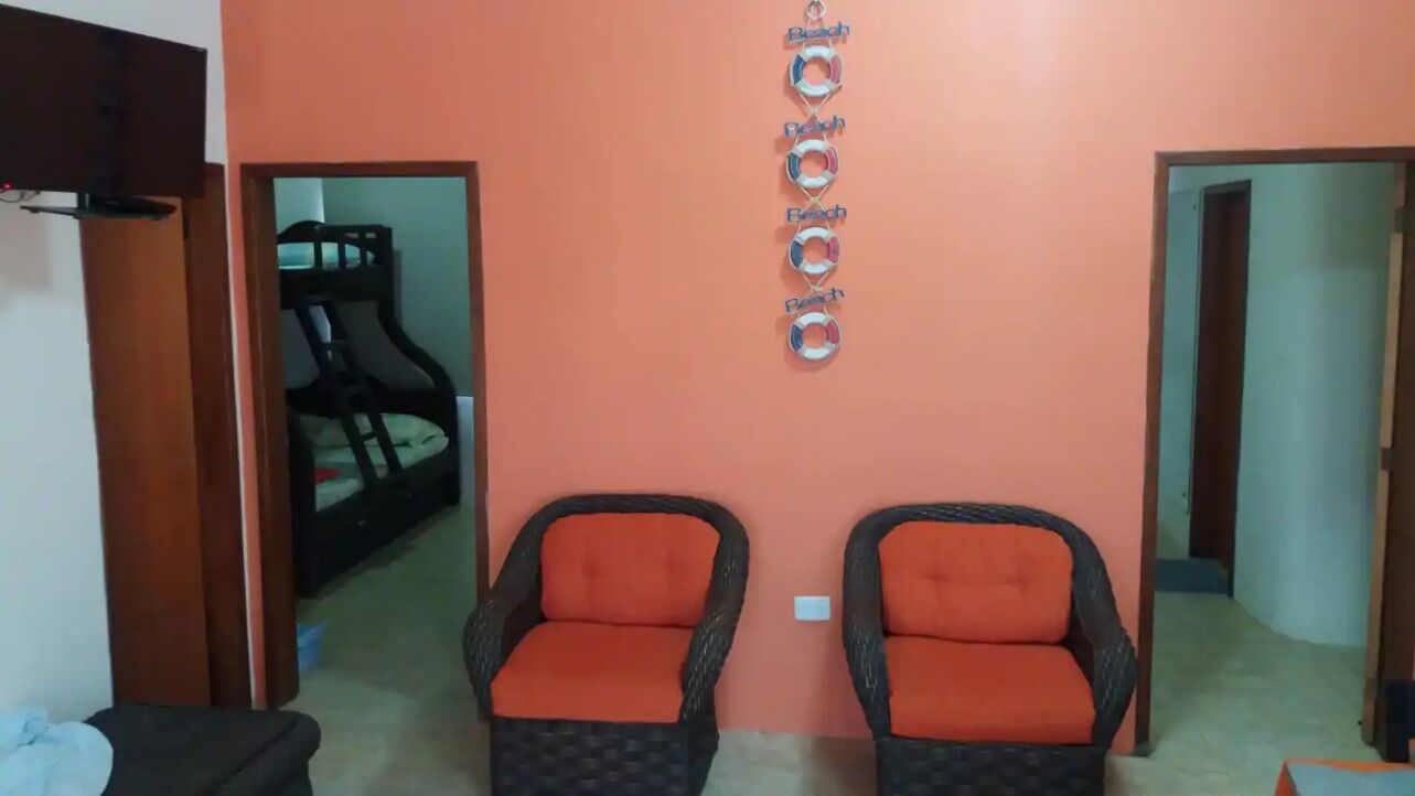 A room with two wicker chairs with orange cushions, a wall with a circular decoration, and a bunk bed in the background.