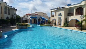 A swimming pool area with a clear blue pool, surrounded by buildings with arched windows and balconies. - Family-sized condo with pool and beatiful areas (Chichiriviche)