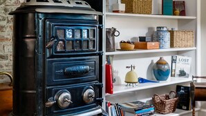A vintage black stove with a chimney, a white brick wall, and a white shelving unit with various decorative items. - Historic headquarters of city founder! Gated parking! (Saint Charles)
