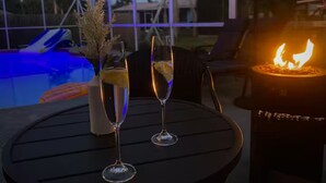 Een zwembadterras met een tafel, twee drankglazen, een decoratieve vaas en een vuurplaats.