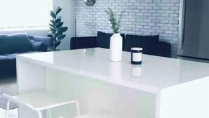 Een moderne keuken met een wit kookeiland, twee witte barkrukken en een accentmuur van baksteen.
