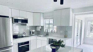 Een moderne keuken met witte kasten, roestvrijstalen apparatuur en een centraal eiland met een potplant.