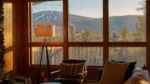 A cozy cabin interior with a large window offering a view of a mountainous landscape. - Stratton Chalet | Barrel Sauna, Hot Tub & Views (Winhall)