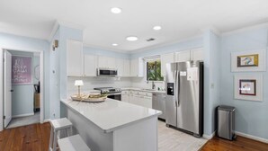 Une cuisine moderne avec des meubles blancs, un îlot central, des appareils en acier inoxydable et une petite poubelle.