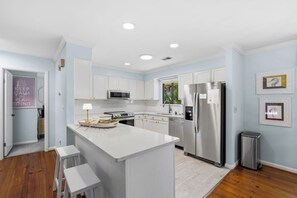 Una cocina moderna con armarios blancos, una isla central, electrodomésticos de acero inoxidable y un cubo de basura pequeño.