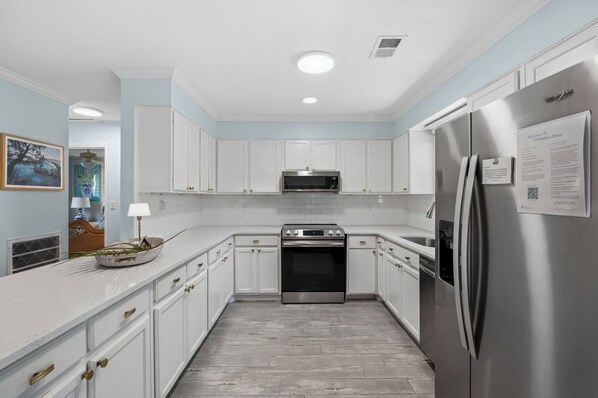 A modern kitchen with white cabinetry, stainless steel appliances, and a tiled backsplash. - Captain’s Corner, 379 Wahoo Drive (Fripp Island)