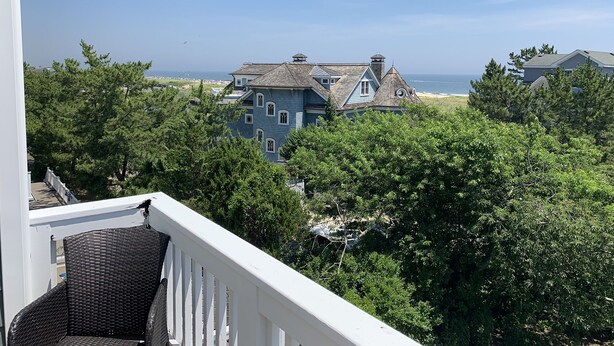 Ein großes Haus mit blauer Fassade, umgeben von dichten, grünen Bäumen, mit Blick auf einen Strand.