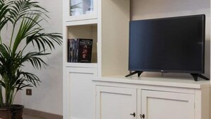 A room with a flat-screen TV on a white cabinet, a potted plant, and a shelf with books. - Fiesole is Magic (Fiesole)