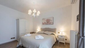 A bedroom with a bed, bedside tables, a chandelier, a radiator, and a door. - Fiesole is Magic (Fiesole)