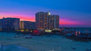A beachfront hotel with multiple high-rise buildings, a sandy beach, and a sunset sky.
