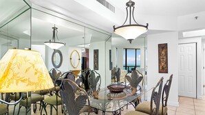 A dining area with a glass table surrounded by ornate metal chairs, a glass partition, and a view of the ocean through large windows.