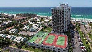 A high-rise hotel with a tennis court and a beach view.