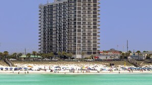 A high-rise hotel with multiple balconies, located near a beach with umbrellas and people.