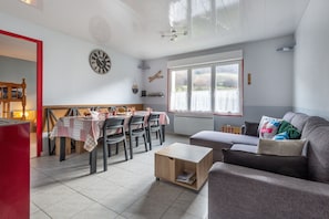 Uma sala de estar moderna com área de jantar, um sofá cinza e uma mesa de madeira com cadeiras.