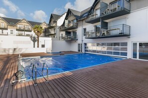 Ein Schwimmbad mit Holzterrasse, umgeben von mehrstöckigen Gebäuden mit Balkonen.