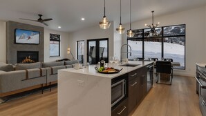 A modern kitchen with a central island, large windows with a snowy view, and a cozy seating area with a fireplace.