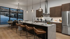 A modern kitchen with a large island, bar stools, stainless steel appliances, and a view of a snowy landscape.